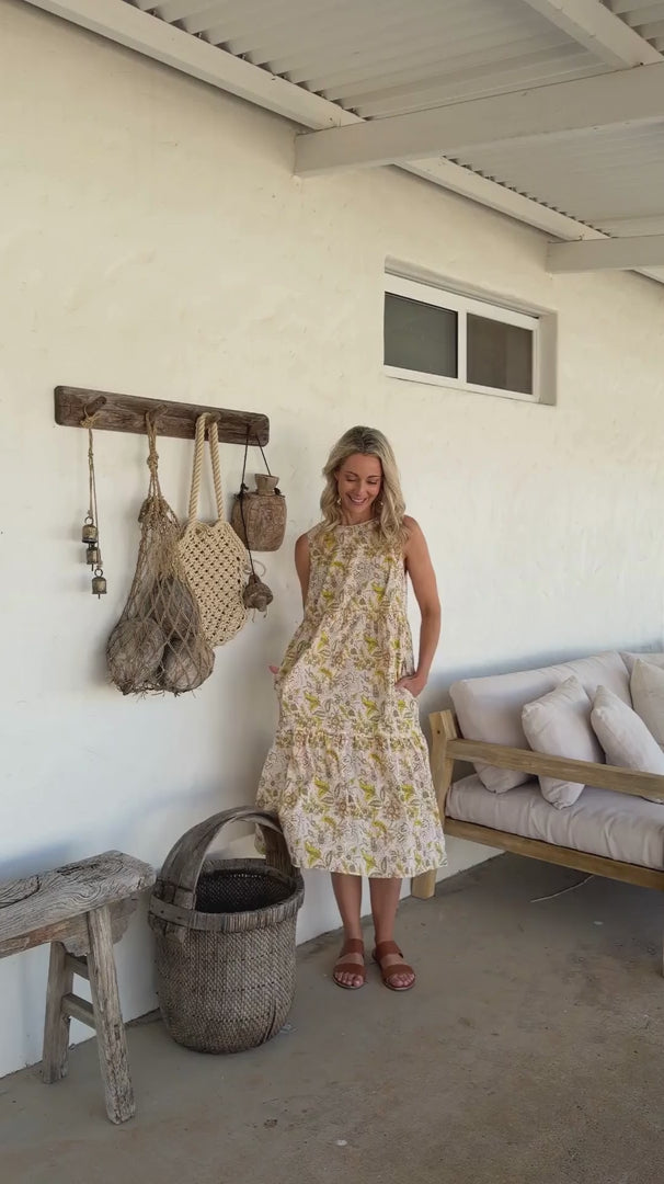 Video of a model wears 100% cotton sleeveless midi dress with high round neckline, tiered design and pockets in cream based floral print