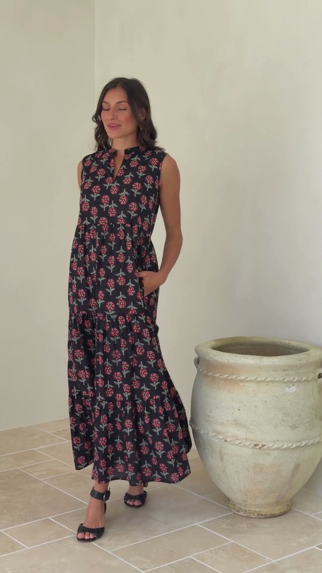 Video of woman wearing a 100% cotton black floral tiered maxi dress with sleeveless design and notch neckline. 