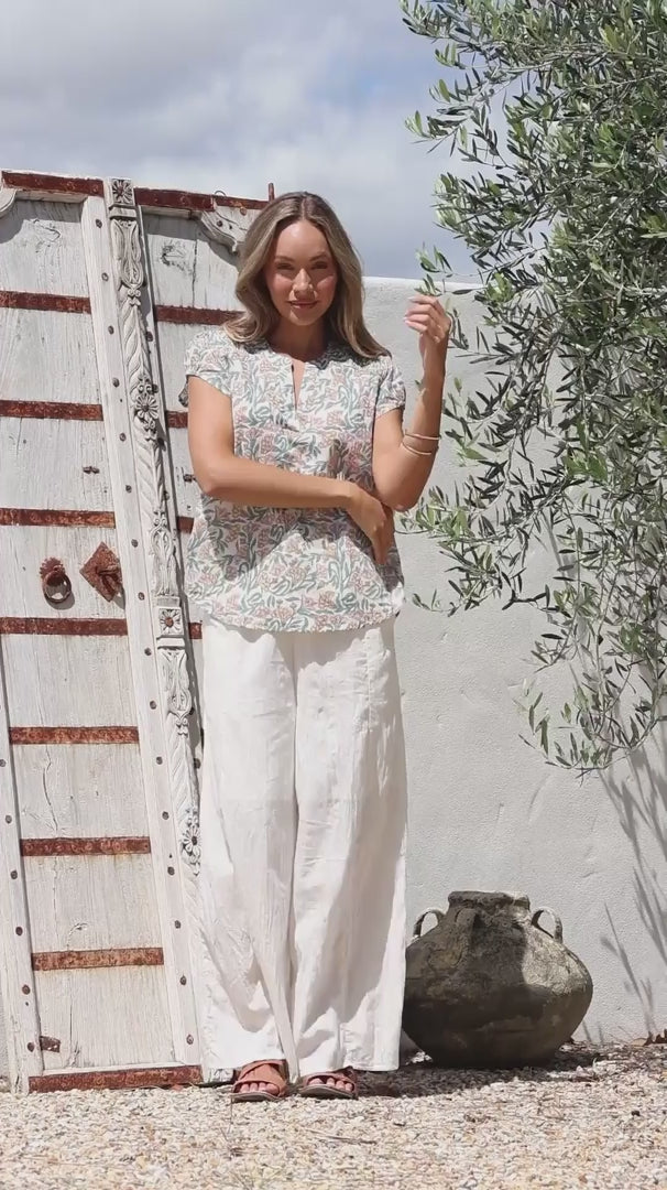 Video of a woman wearing a 100% cotton white based floral top paired with a plain white pants