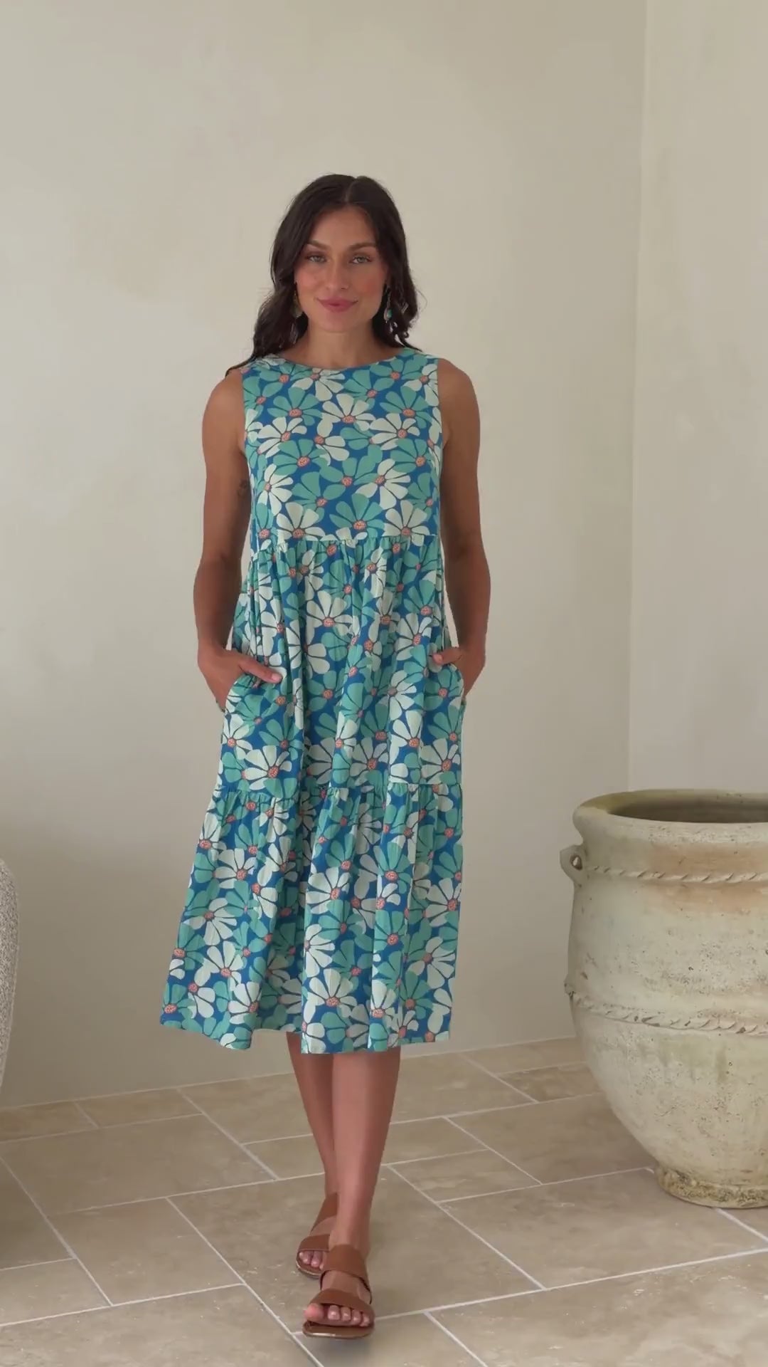Video of a woman wearing a cotton sleeveless three tiered midi length dress in aqua and royal blue daisy print.
