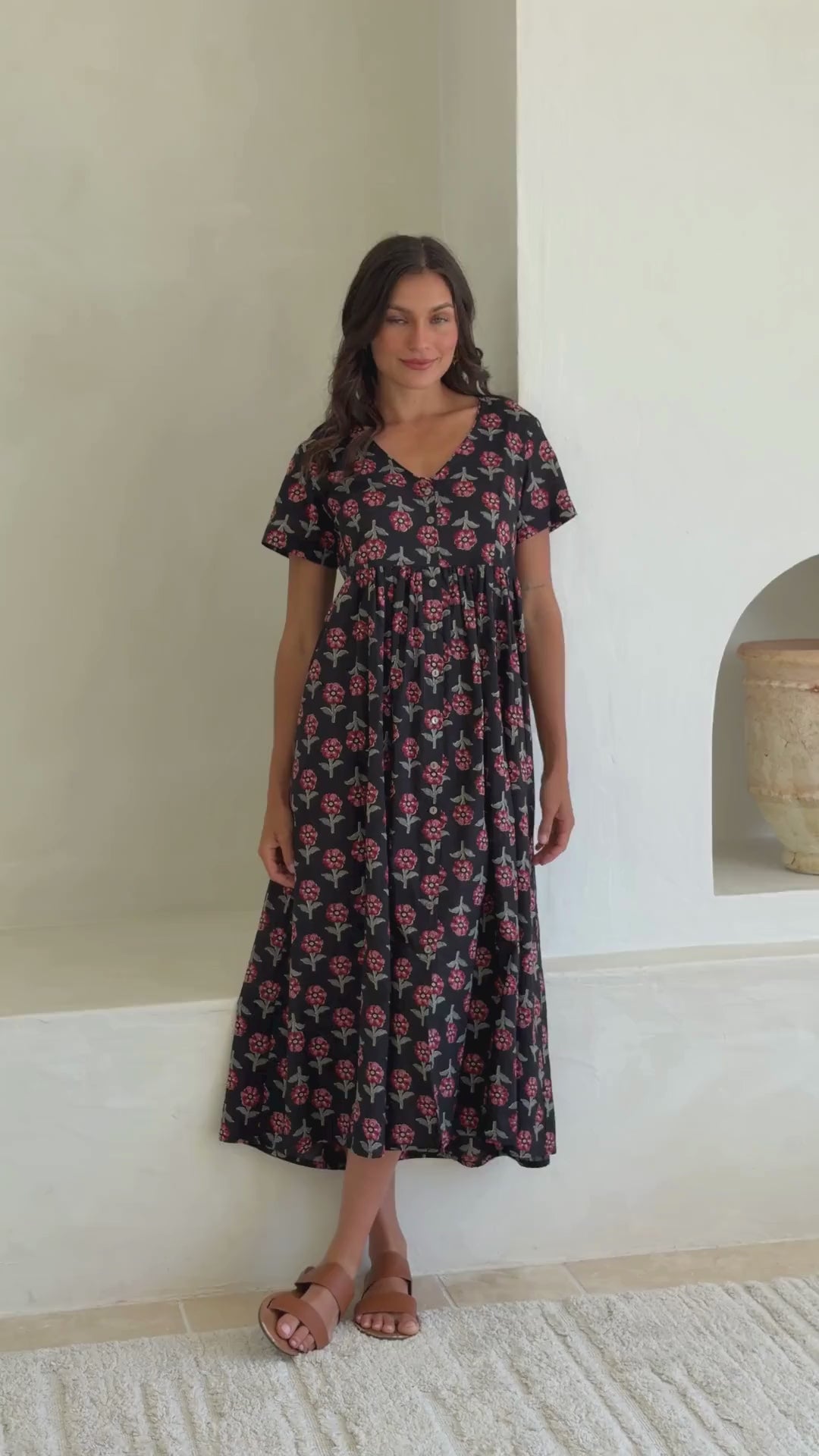 Video of woman wearing in a 100% cotton floral print dress with a V-neckline, short sleeves, pockets, and buttons through to the knee.