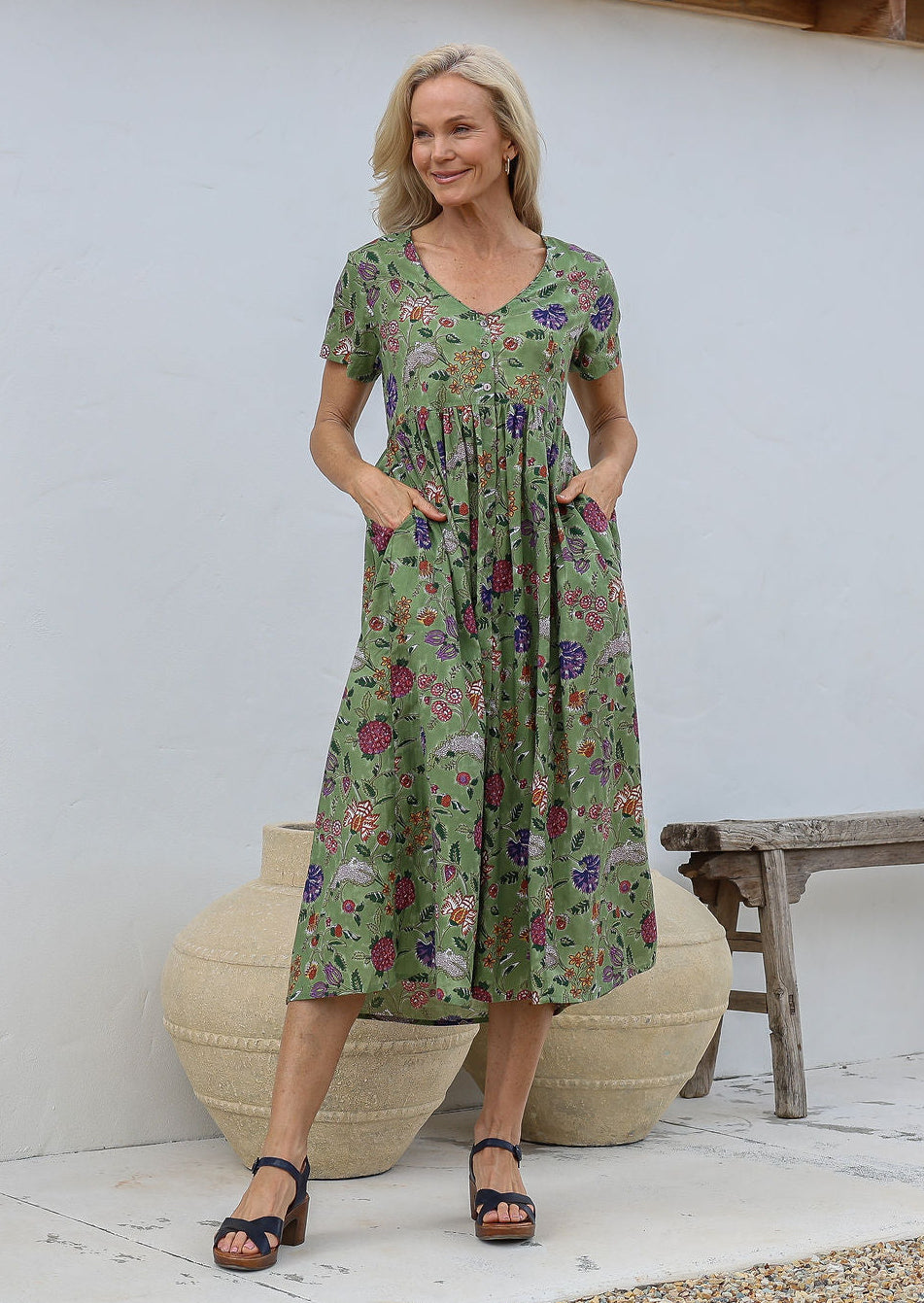 Woman standing with both the hands in pockets wearing a relaxed fit midi length cotton dress with empire waistline and gathered design.