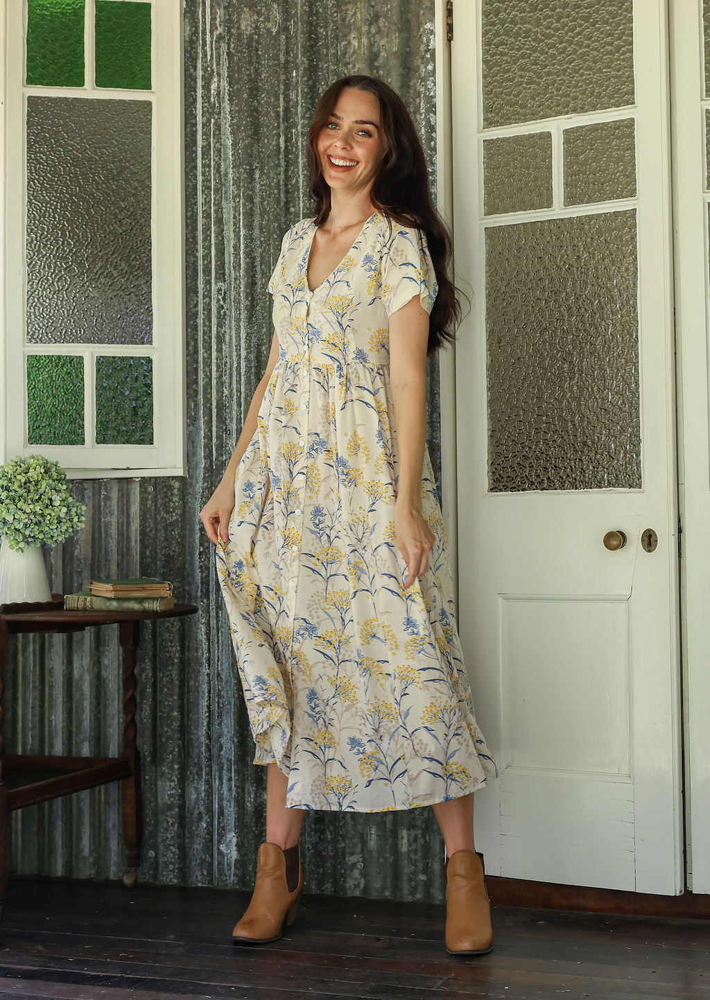 Woman in a white floral cotton maxi dress with full skirt  standing on a verandah of a rustic cottage