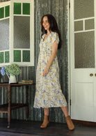 Woman in a white floral pure cotton maxi dress standing on a verandah of a rustic cottage