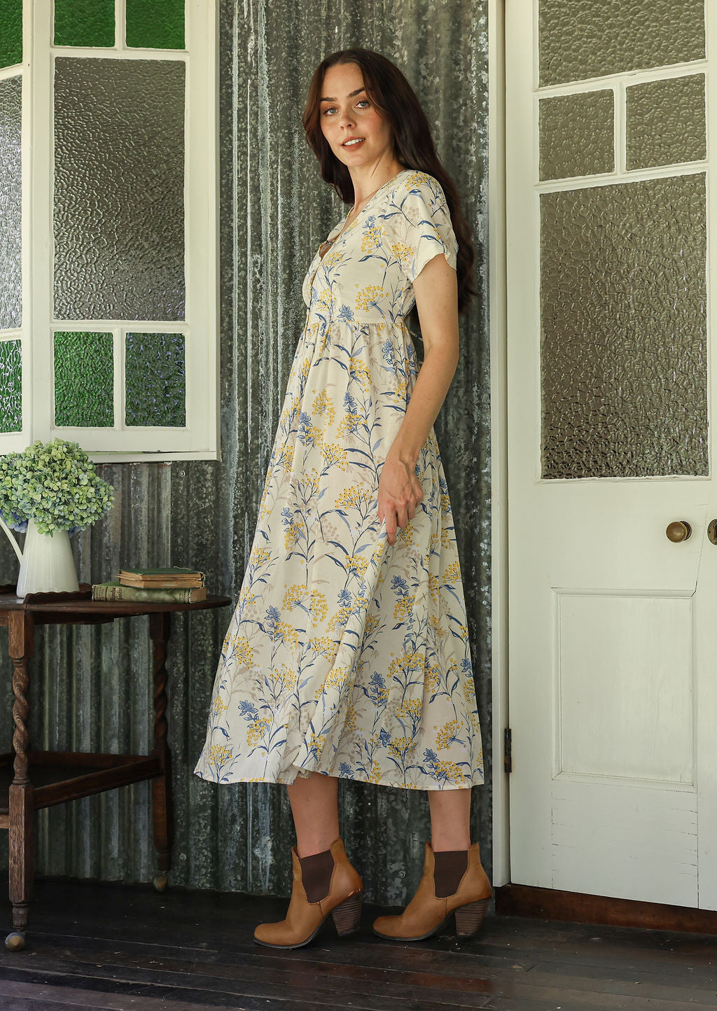 Woman in a white floral cotton dress with v neck standing on a verandah of a rustic cottage