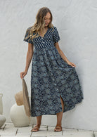Woman standing in a 100% cotton floral print dress with a V-neckline, short sleeves, pockets, and buttons through to the knee.