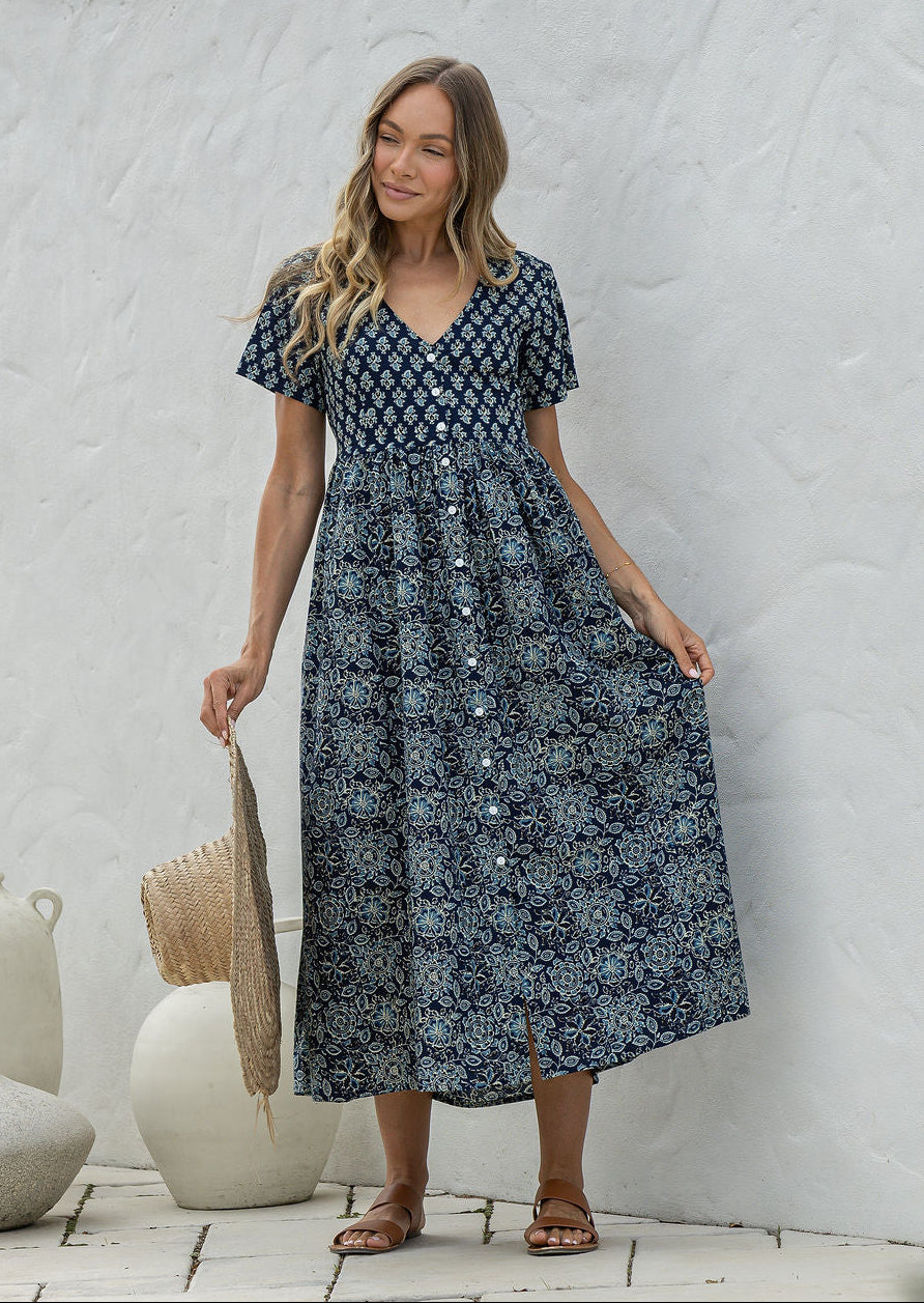 Woman wearing a relaxed fit, button through cotton dress in navy blue base floral print with V neckline.
