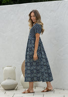 Woman stands sideways wearing a 100% cotton dress with short sleeves, pockets, and a drawstring tie at the back.