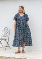 Woman posing in a relaxed fit, short sleeved, floral cotton dress with V- neckline, drawstring waist tie and pockets 