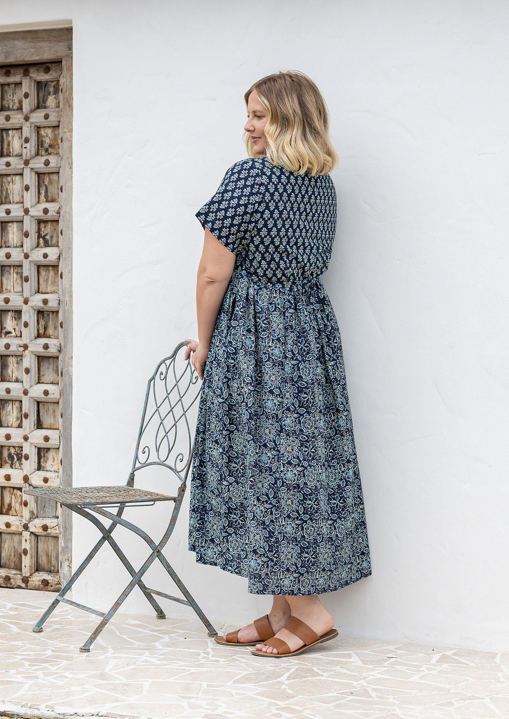 Woman stands sideways wearing a relaxed fit, button through cotton dress in navy blue base floral print with V neckline.