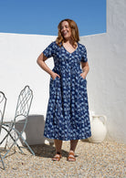 Woman posing in a relaxed fit, short sleeved, floral cotton dress with V- neckline, drawstring waist tie and pockets 