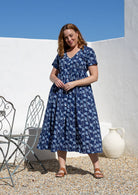 Woman wearing a relaxed fit, button through cotton dress in navy blue base floral print with V neckline.