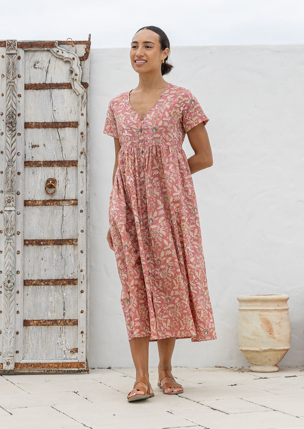 Woman wearing a relaxed fit, button through cotton dress in rose pink base floral print with V neckline.