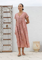 Woman wearing a relaxed fit, button through cotton dress in rose pink base floral print with V neckline.