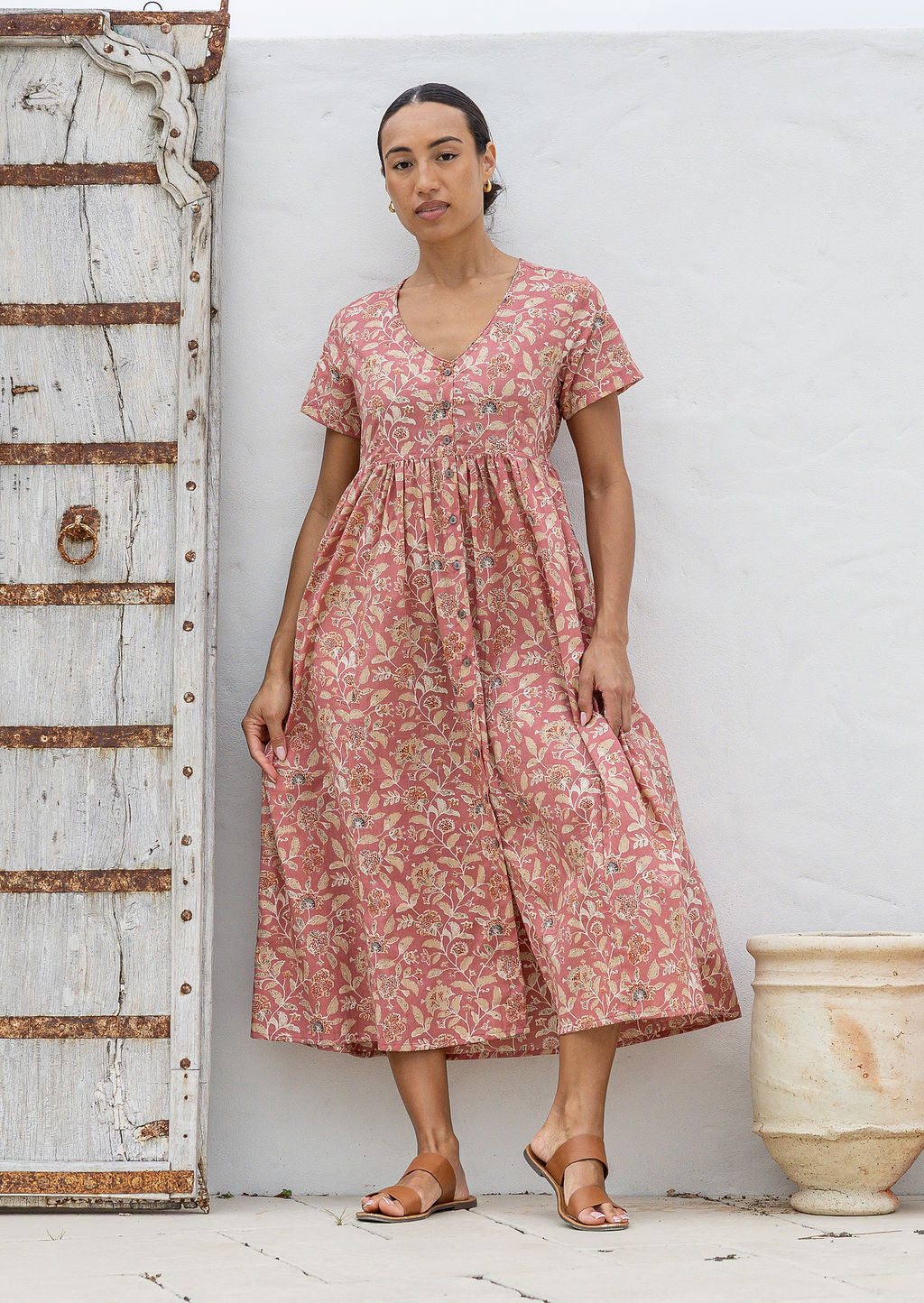 Woman standing in a 100% cotton floral print dress with a V-neckline, short sleeves, pockets, and buttons through to the knee.