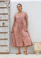 Woman standing in a 100% cotton floral print dress with a V-neckline, short sleeves, pockets, and buttons through to the knee.