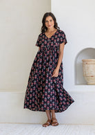 Woman posing in a relaxed fit, short sleeved, floral cotton dress with V- neckline, drawstring waist tie and pockets 