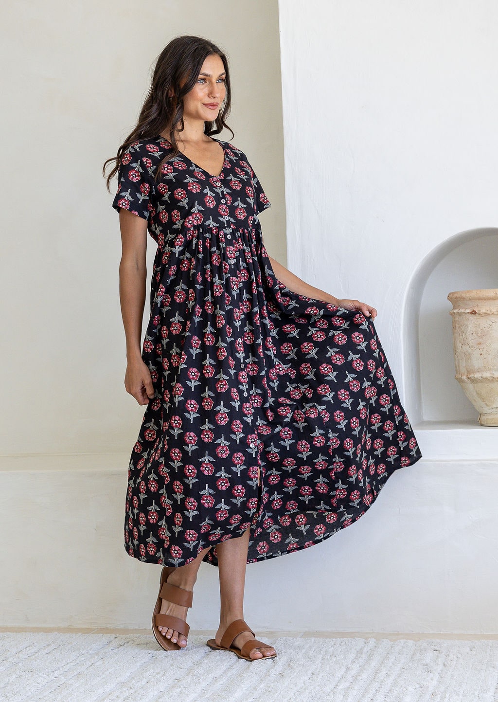 Woman wearing a cotton Black floral maxi dress with short sleeves and V-neck skirt held out to show flare.