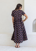 Woman stands backwards wearing a 100% cotton dress with short sleeves, pockets, and a drawstring tie at the back.