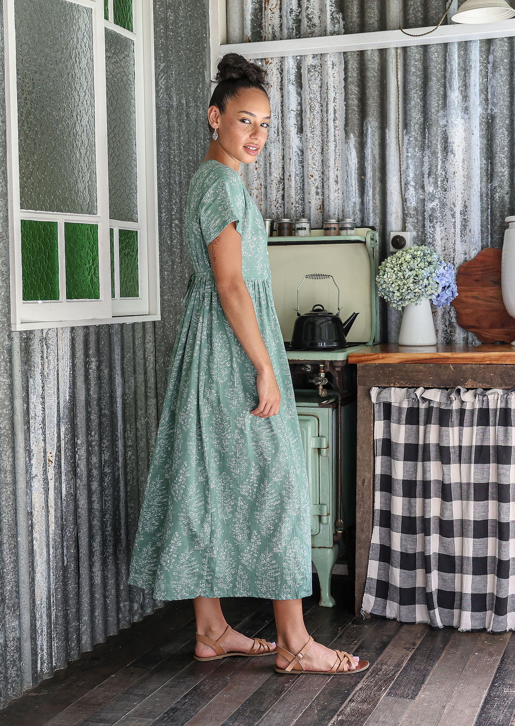 Woman stands sideways wearing a 100% cotton dress with short sleeves, pockets, and a drawstring tie at the back.