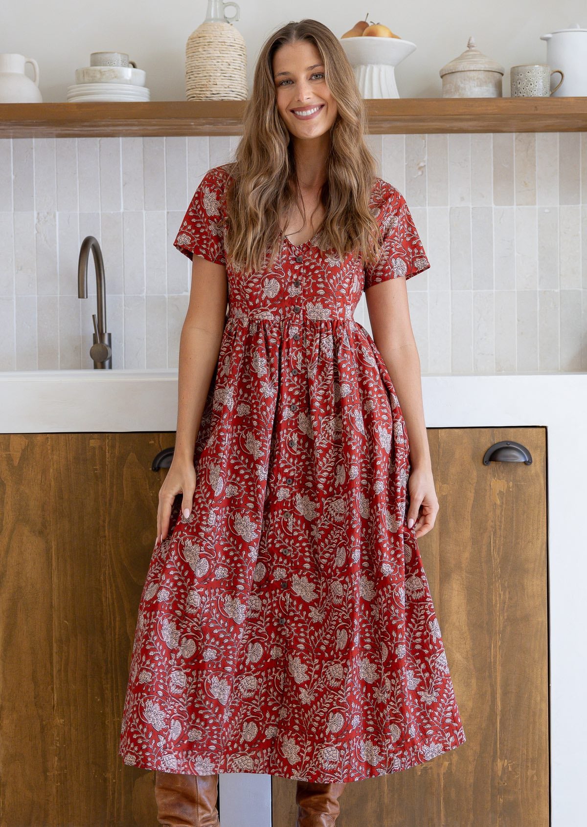 Woman standing in a 100% cotton floral print dress with a V-neckline, short sleeves, pockets, and buttons through to the knee.