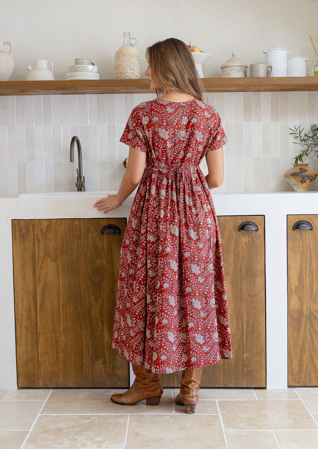 Woman stands backwards wearing a 100% cotton dress with short sleeves, pockets, and a drawstring tie at the back.