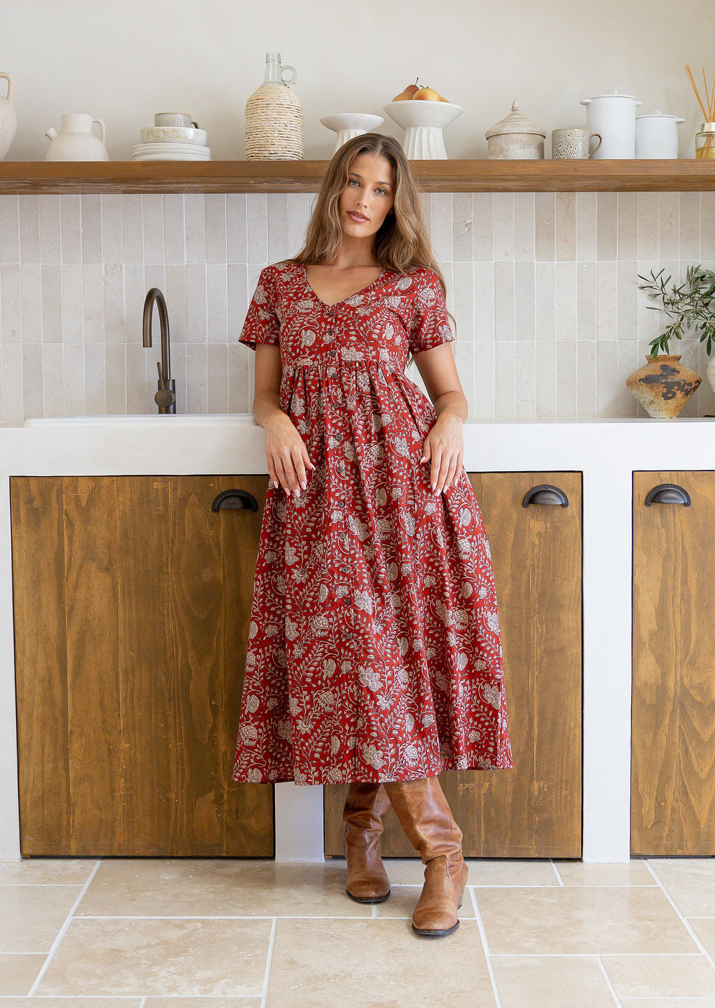 Woman wearing a relaxed fit, button through cotton dress in red base floral print with V neckline.