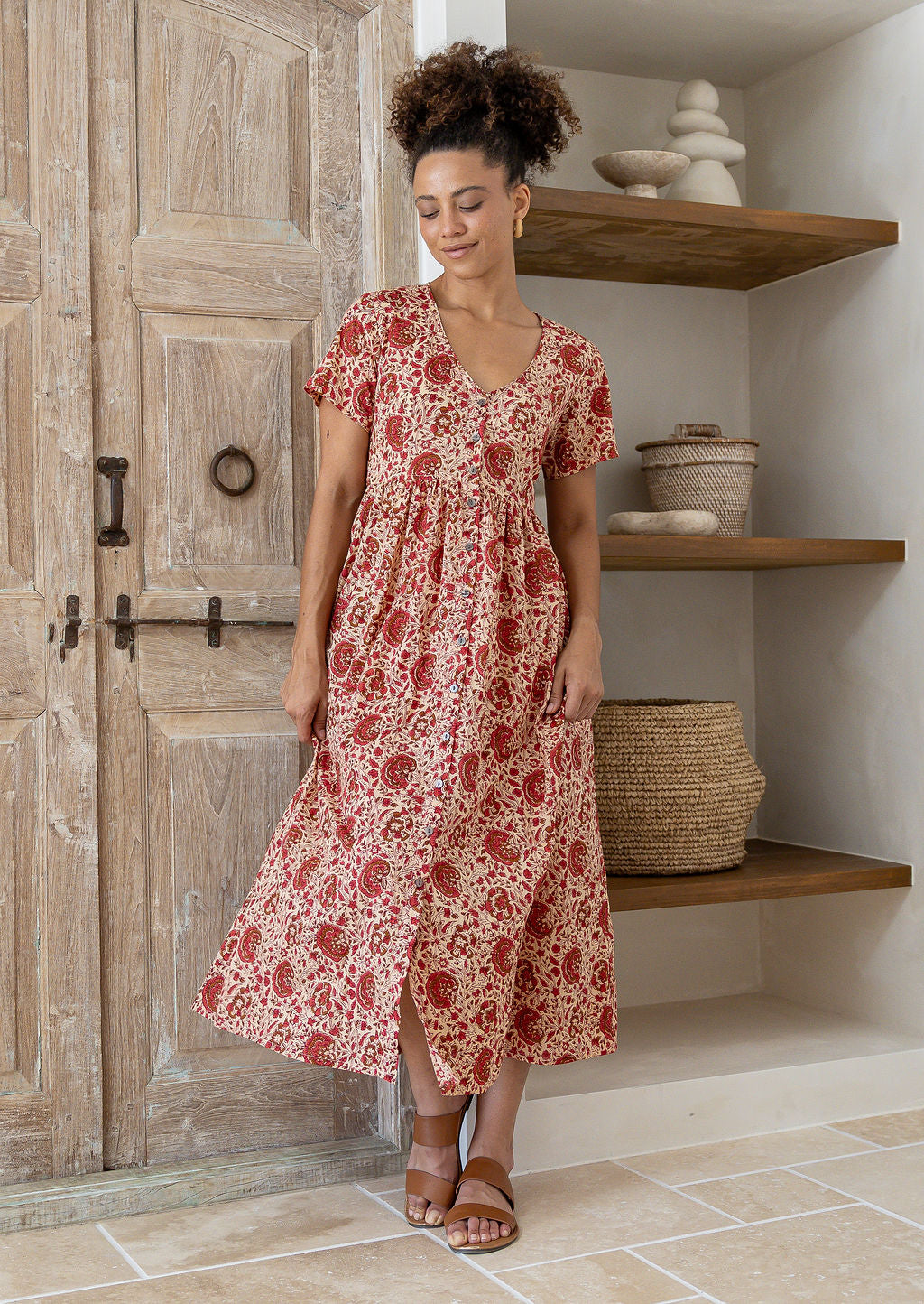 Woman standing in a 100% cotton floral print dress with a V-neckline, short sleeves, pockets, and buttons through to the knee.