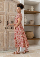 Woman stands sideways wearing a 100% cotton dress with short sleeves, pockets, and a drawstring tie at the back.