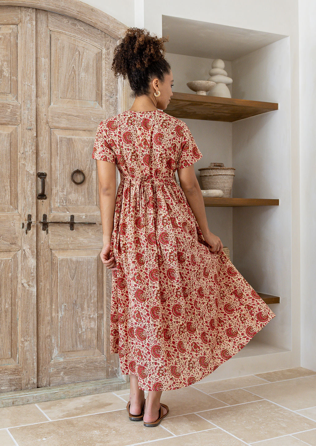 Woman stands backwards wearing a 100% cotton dress with short sleeves, pockets, and a drawstring tie at the back.