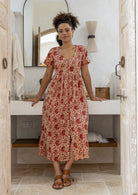 Woman wearing a relaxed fit, button through cotton dress in cream based floral print with V neckline.