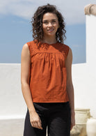 Woman wears rust tone cotton sleeveless top with small gathers across the bust