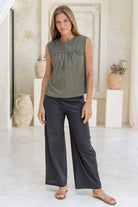 Woman wears olive green 100%  cotton sleeveless top with small gathers across the bust and high round neckline.