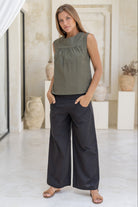 Woman wears cotton sleeveless top in olive green with gathers under the square neckline yoke.