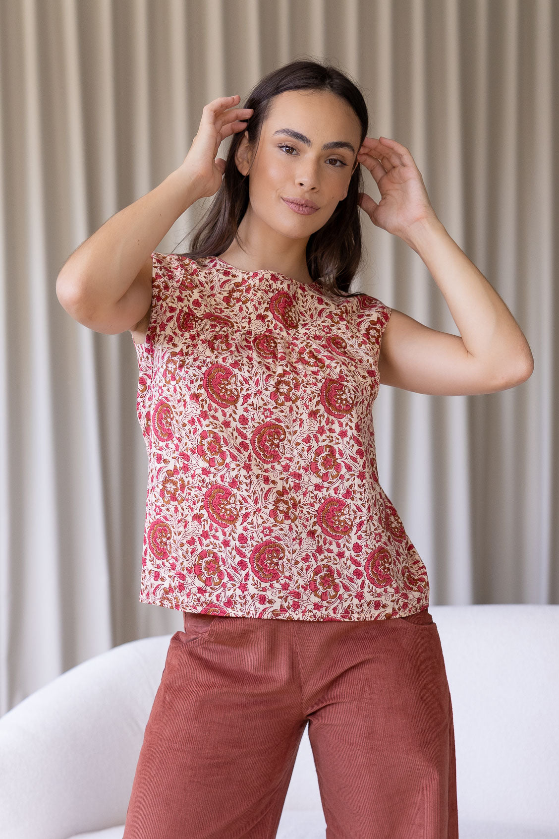 Woman wears cotton sleeveless top in sweet floral print on gentle cream base, with gathers under the square neckline yoke