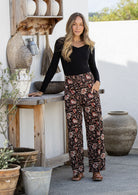 Woman wearing a black top and black based floral print cotton pants standing outdoors.