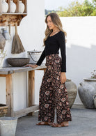 woman stands sideways wearing a 100% cotton pant in black based floral print paired with a basic top