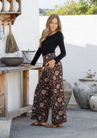Woman wearing a black top and black floral pants standing outdoors.