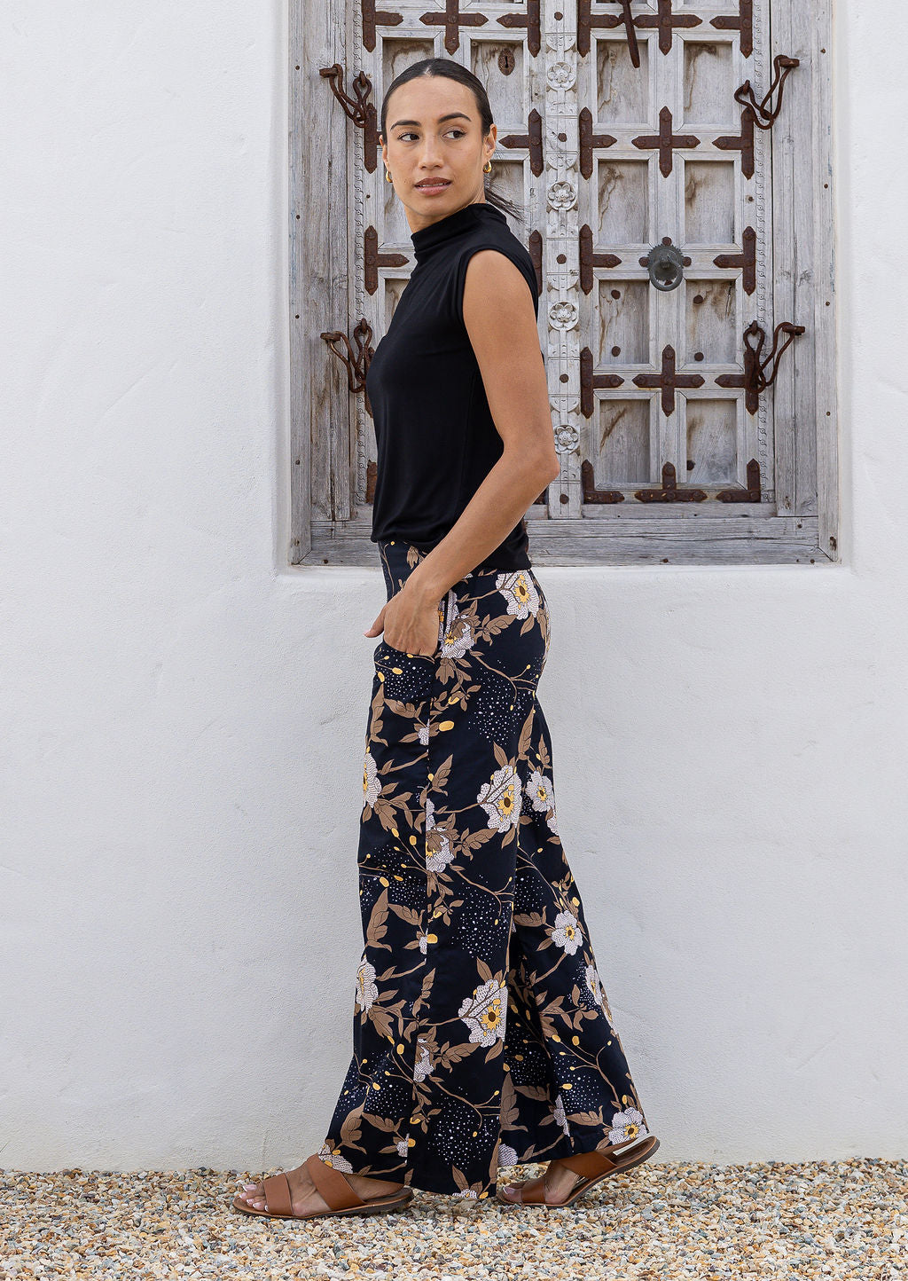 Model poses in black floral cotton pants with side zipper, pockets and wide leg fit
