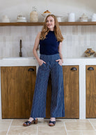 Model poses with both hand in pockets in navy blue based white striped cotton pants with side zipper and wide leg fit
