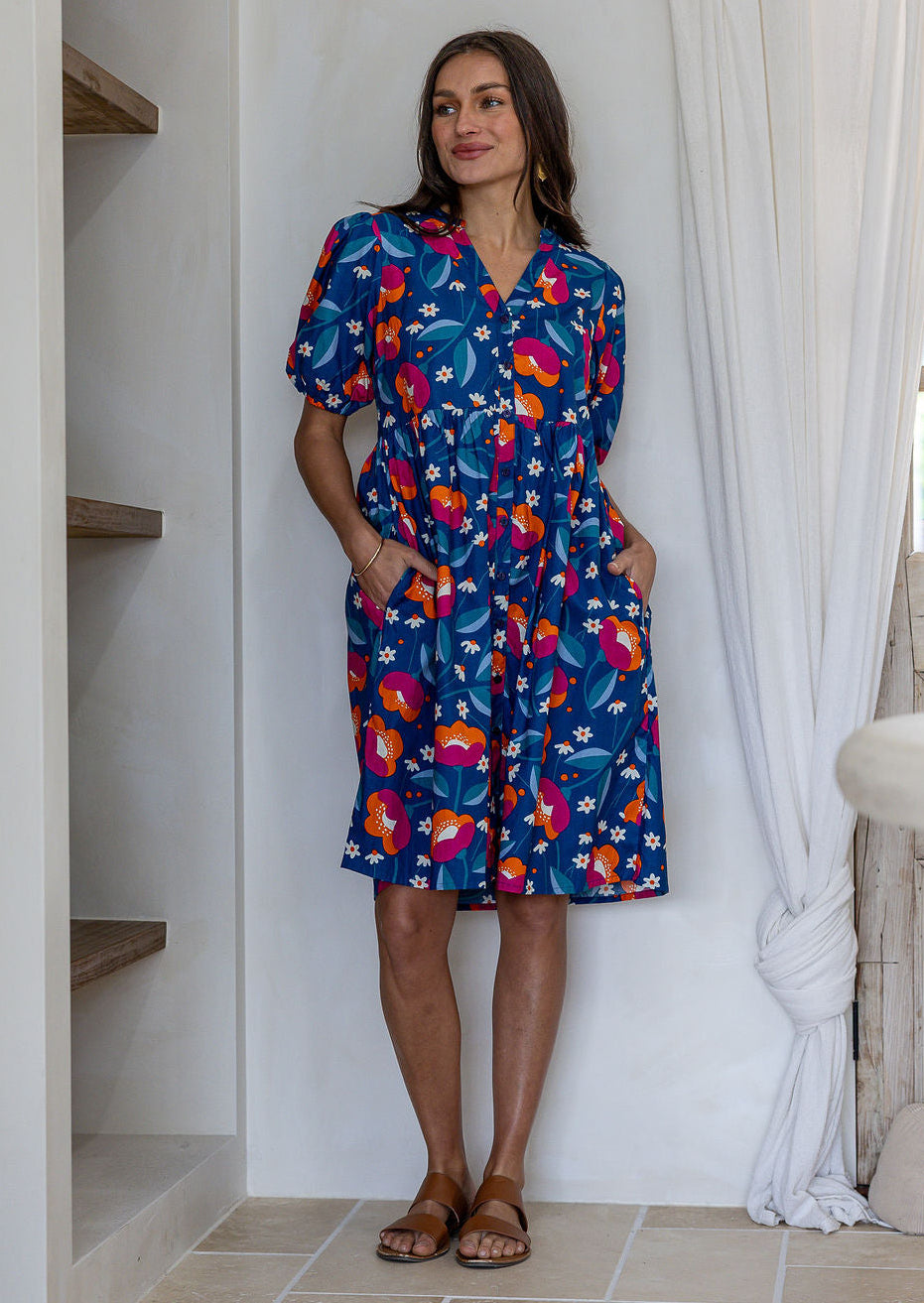 Woman wearing a knee length relaxed fit button through 100% cotton dress with elbow length sleeves and hand in pockets.