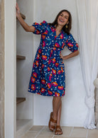 Woman wearing royal blue based floral print 100% cotton dress with, relaxed fit, empire waistline and elasticated elbow length sleeves