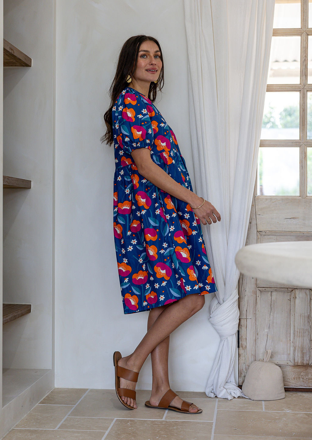 Woman standing sideways wearing a 100% cotton short sleeve dress in royal blue based floral print