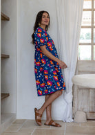 Woman standing sideways wearing a 100% cotton short sleeve dress in royal blue based floral print