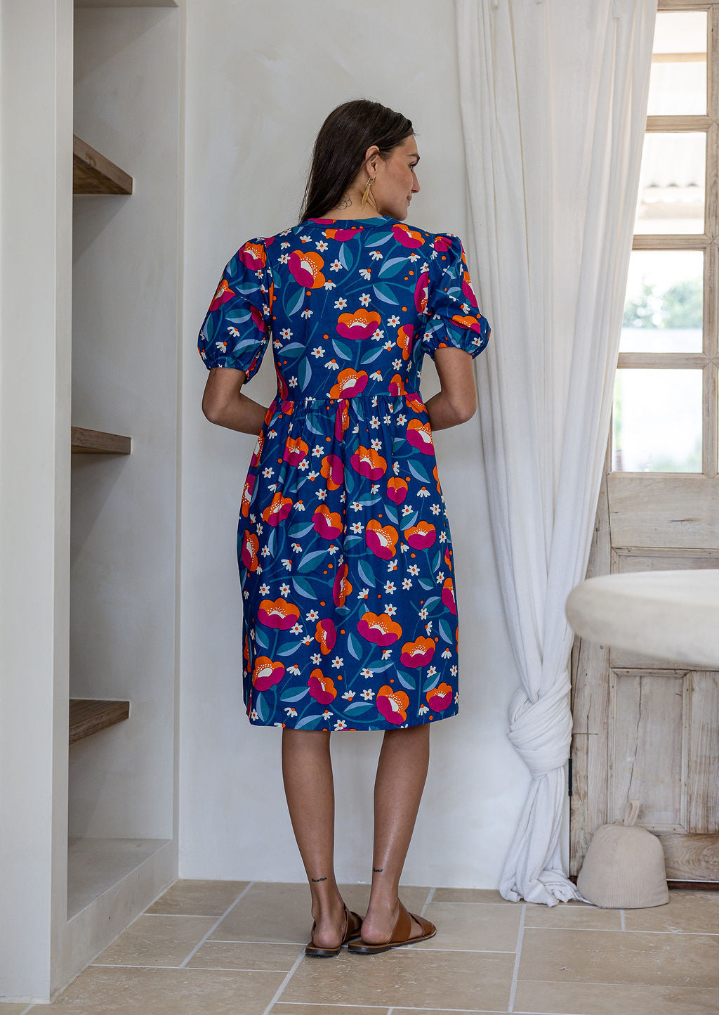 Woman standing backwards wearing a 100% cotton short sleeve dress in royal blue based floral print