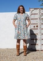Woman wearing a knee length relaxed fit button through 100% cotton dress with elbow length sleeves and hand in pockets.