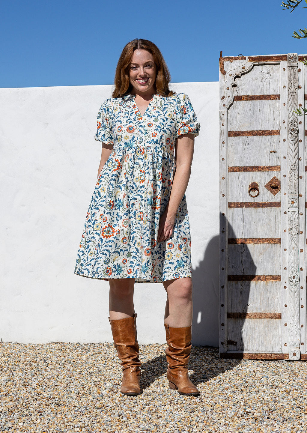 Woman wearing white based floral print 100% cotton dress with, relaxed fit, empire waistline and elasticated elbow length sleeves