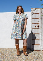 Woman wearing white based floral print 100% cotton dress with, relaxed fit, empire waistline and elasticated elbow length sleeves