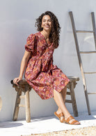 Woman sitting in an outdoor setting wearing a knee length relaxed fit button through 100% cotton dress with elbow length sleeves