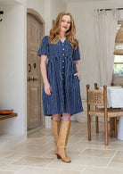 Woman with one hand in pocket wearing a 100% cotton dress with white striped print on a navy base